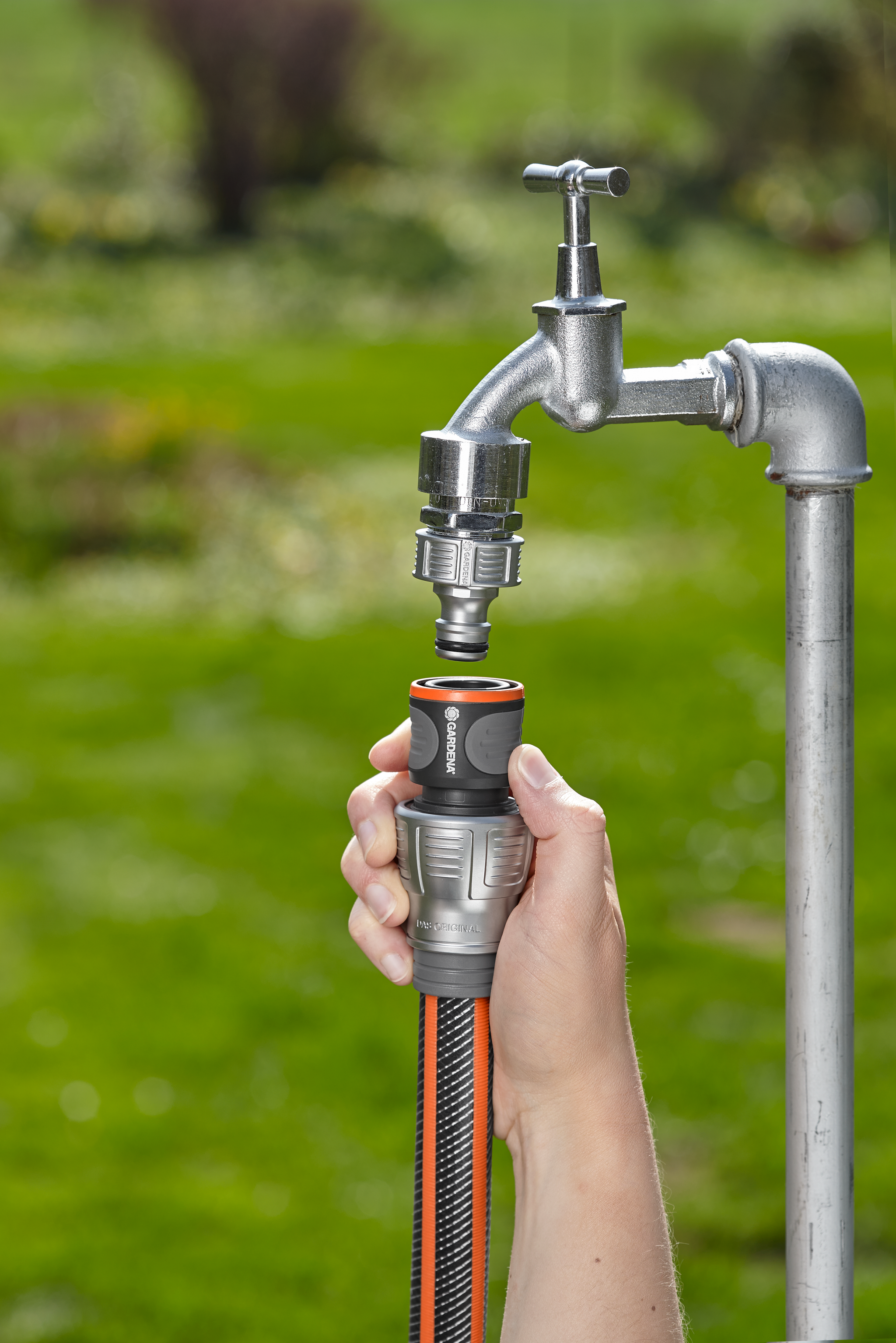A person connecting a Gardena hose to an outdoor water tap in a garden.