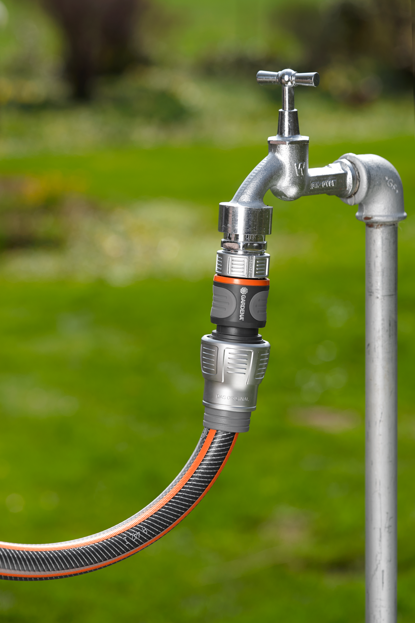 Gardena hose connector attached to an outdoor water tap in a garden setting.