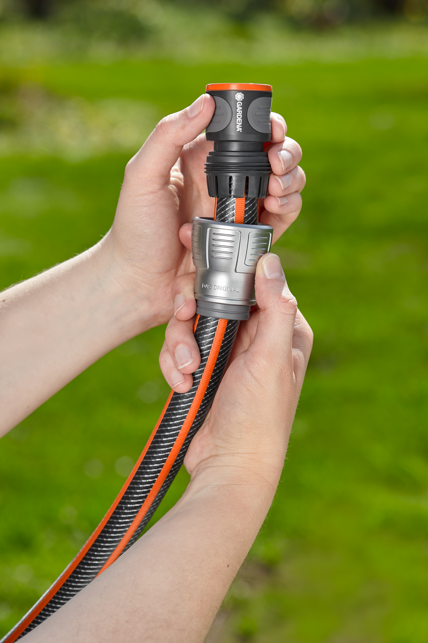 Hands connecting a Gardena hose with a water connector in a garden setting.