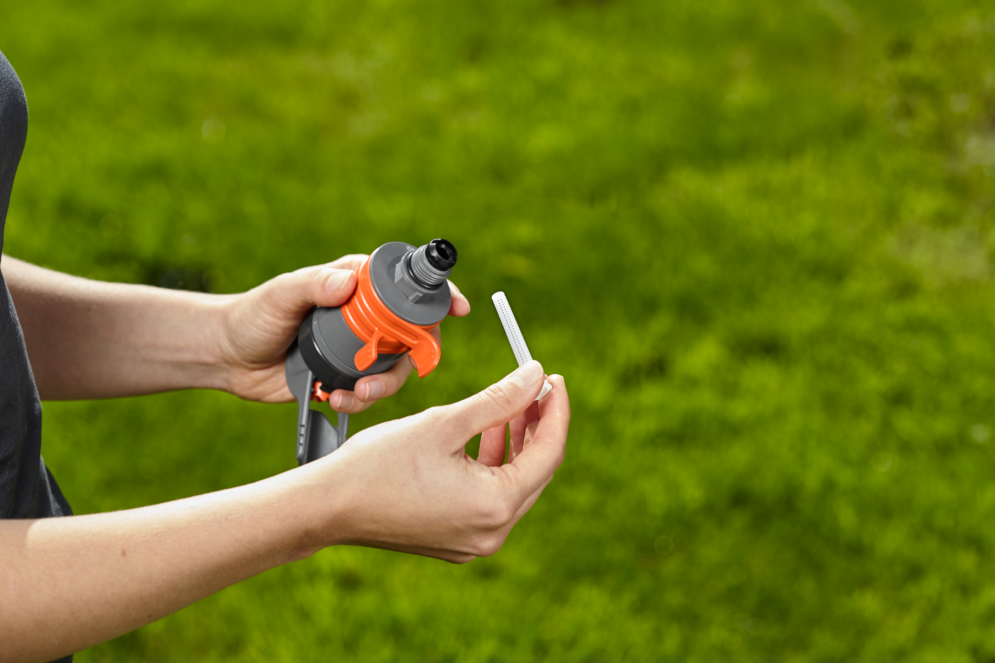 A person holding a Gardena hose nozzle and a small attachment in a garden setting.
