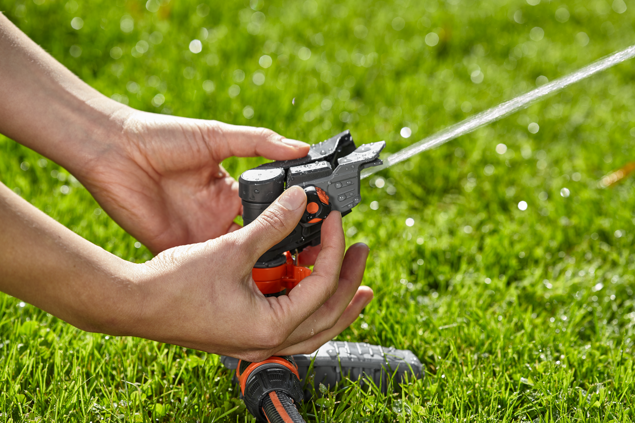 Hands adjusting a garden sprinkler on a lawn.