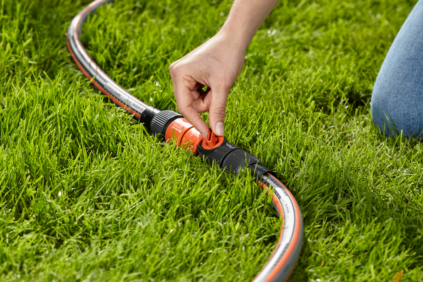 A person adjusting a Gardena hose connector on a garden lawn.