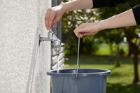 A person filling a bucket with water from an outdoor faucet., miniatuur 5