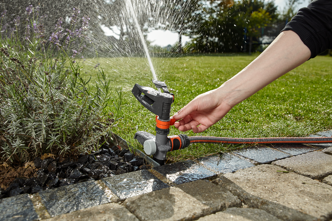 A person adjusting a garden sprinkler in a landscaped garden.