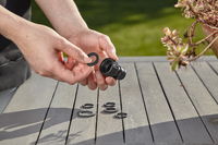 A person holding a garden hose connector with washers on a wooden table., miniatuur 3