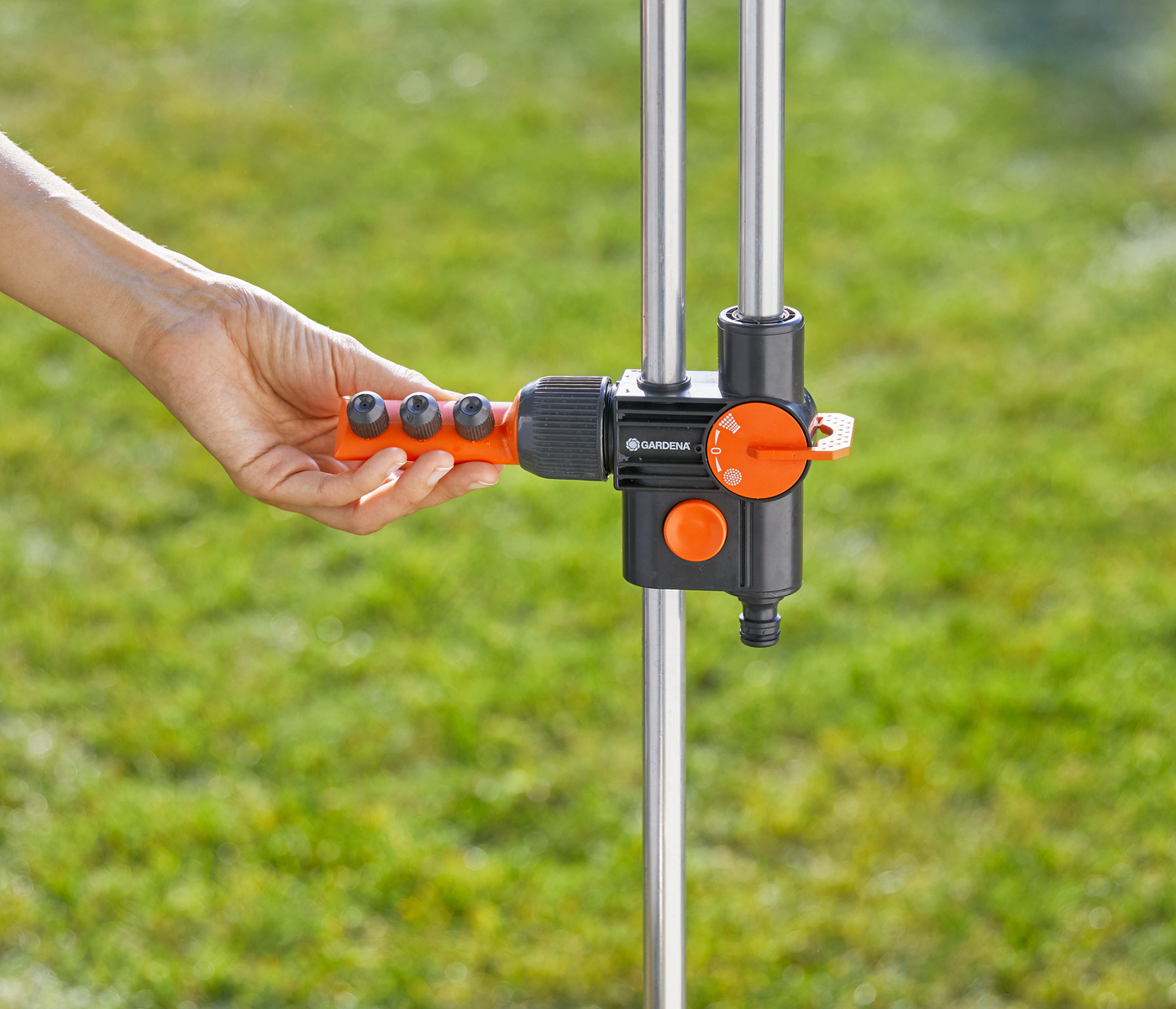 A person adjusting a Gardena water control valve in a garden setting.