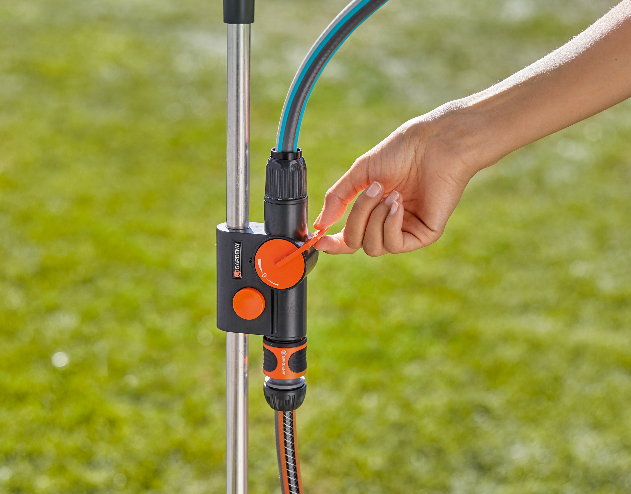 A person adjusting a Gardena water control valve connected to a garden hose.