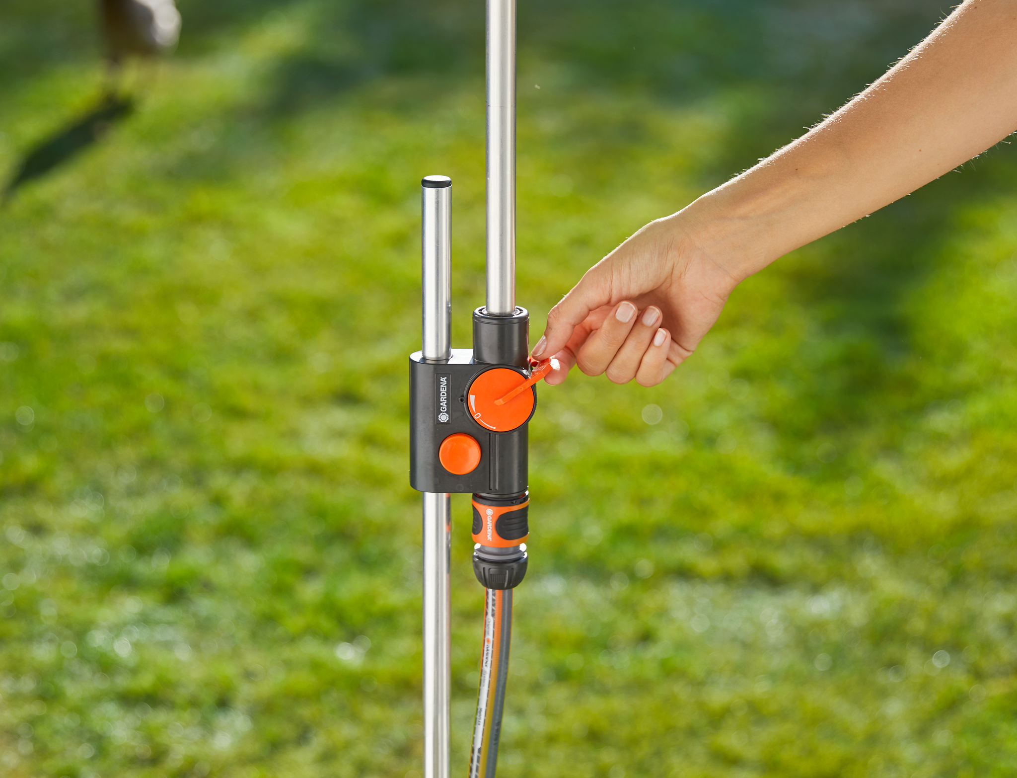 A person adjusting a Gardena water control valve in a garden setting.