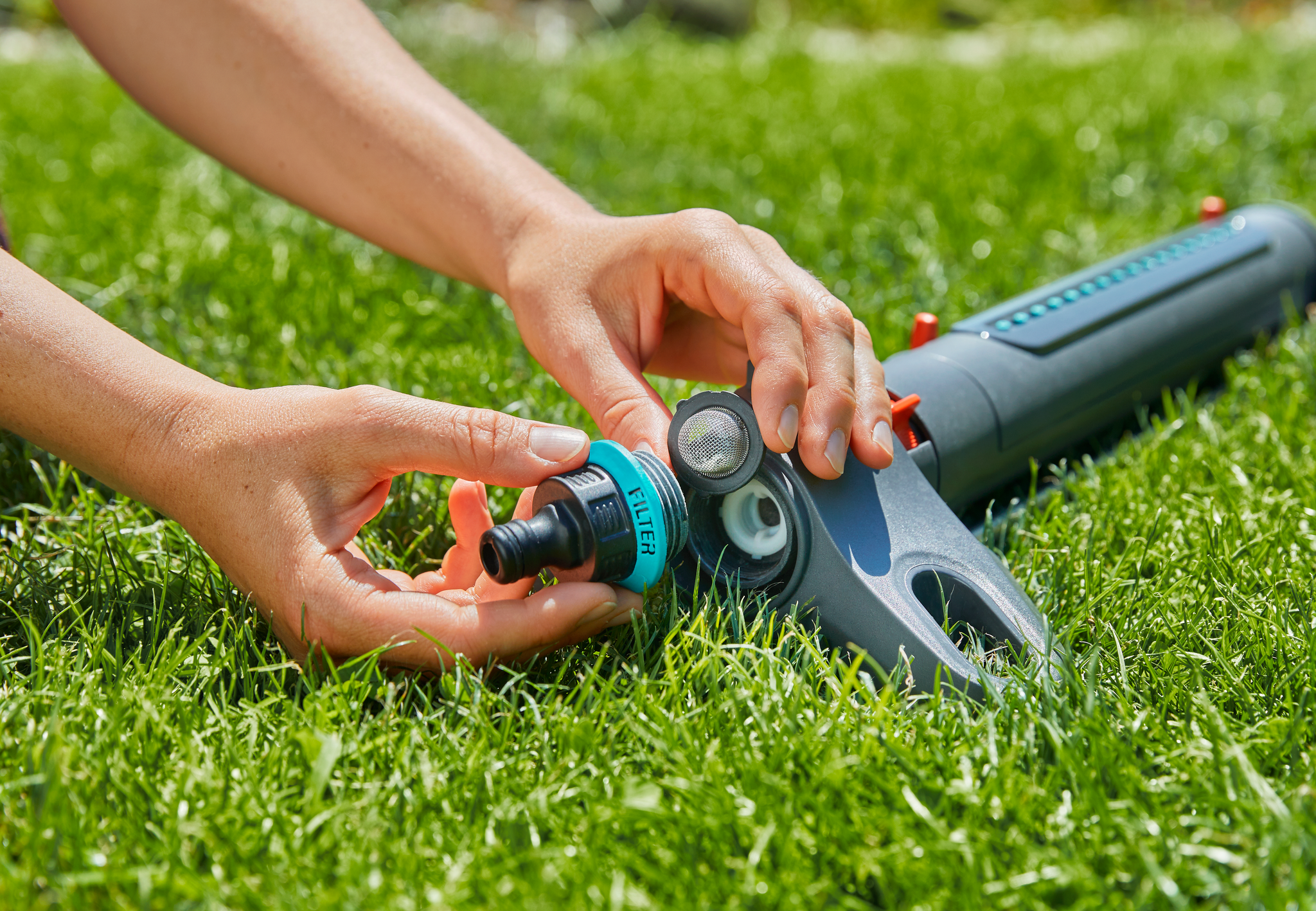 Hands connecting a Gardena hose attachment to a garden sprinkler on grass.