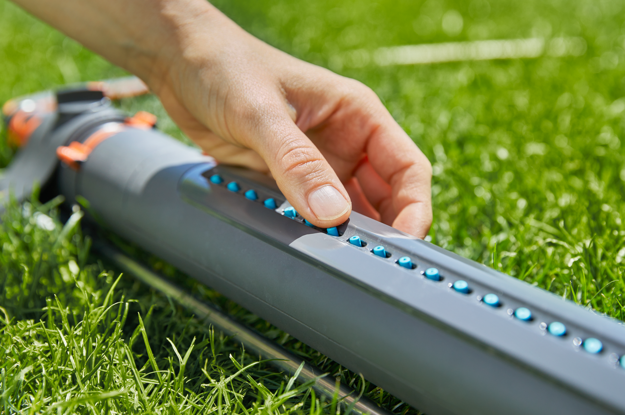 A person adjusting the settings on a garden sprinkler on a lawn.