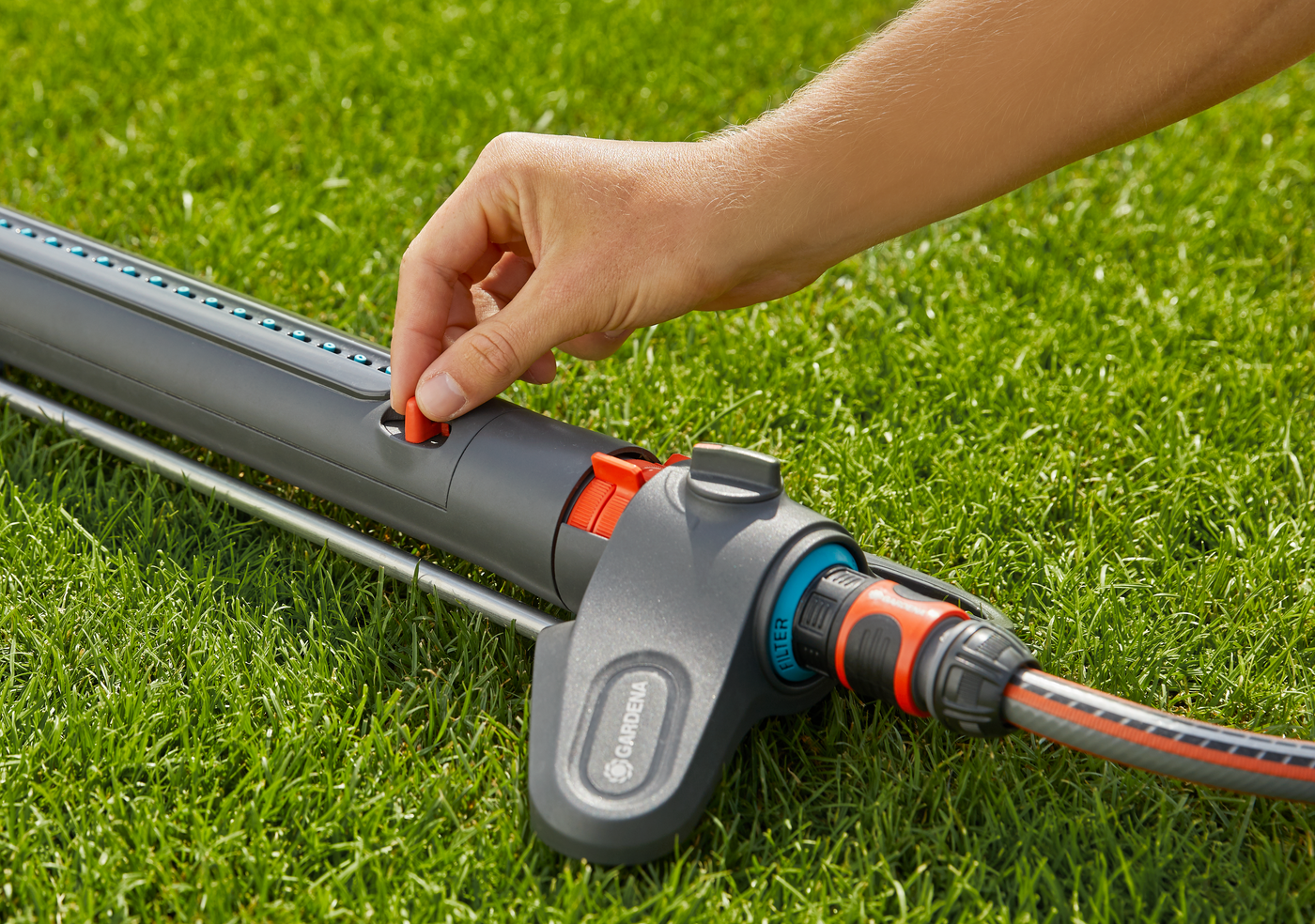 A person adjusting a Gardena garden sprinkler on a grassy lawn.