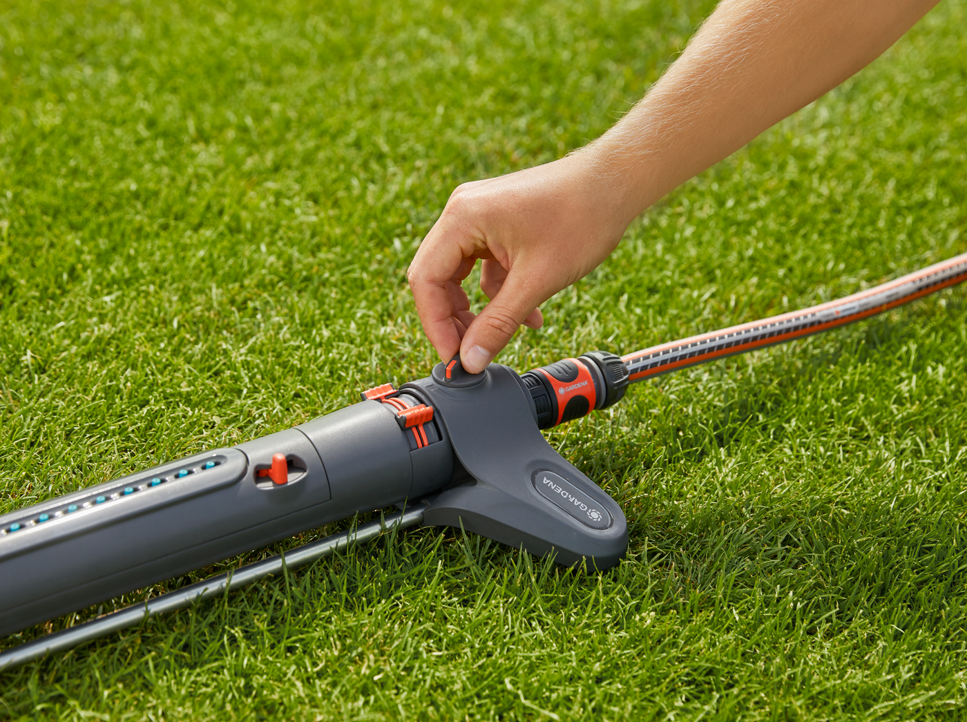 A person adjusting a Gardena garden sprinkler on a lawn.