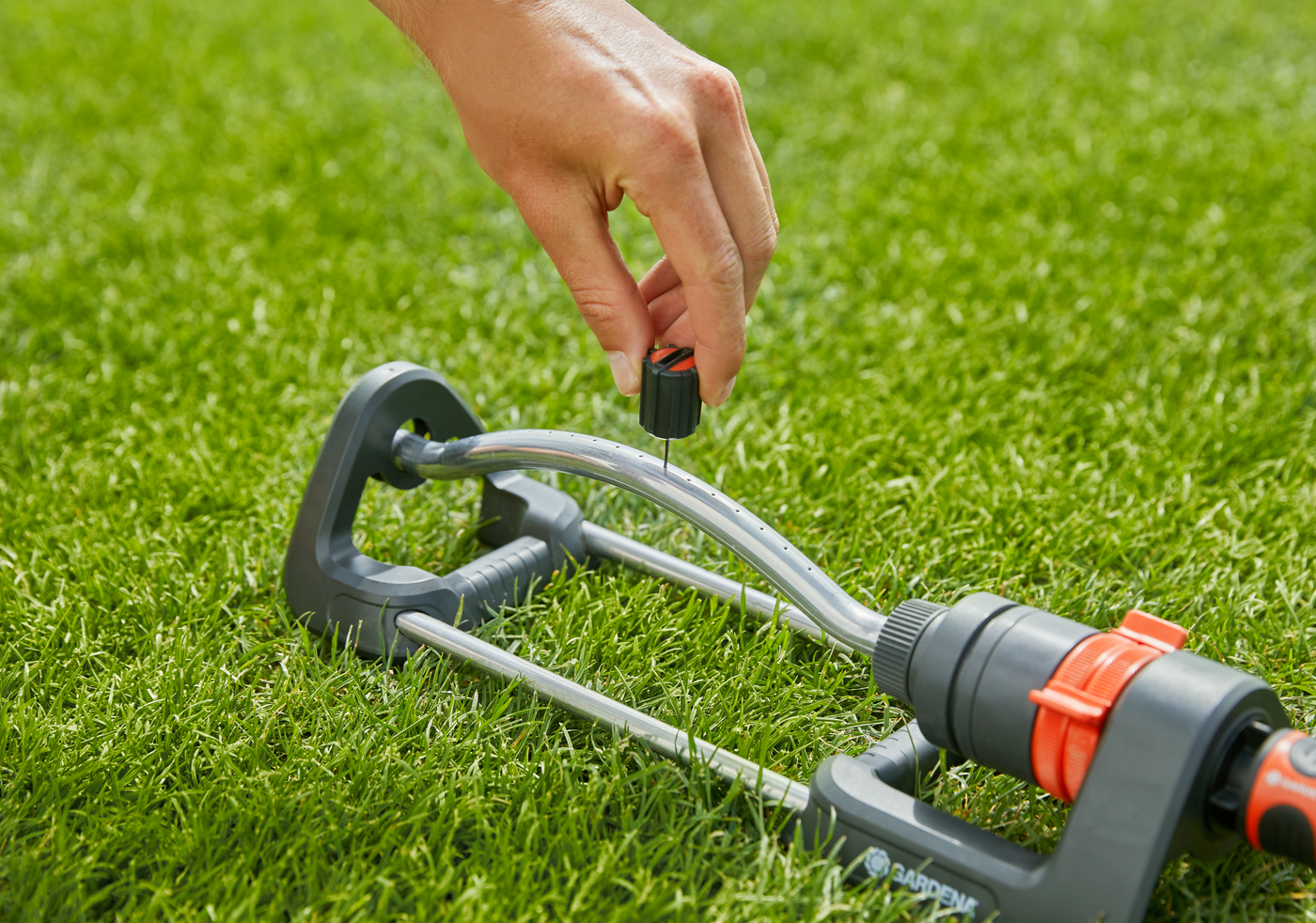 A person adjusting a Gardena garden sprinkler on a lawn.