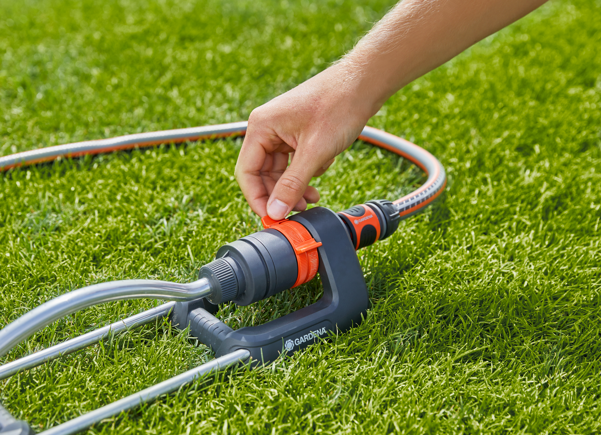 A person adjusting a Gardena garden hose connector on a grassy lawn.