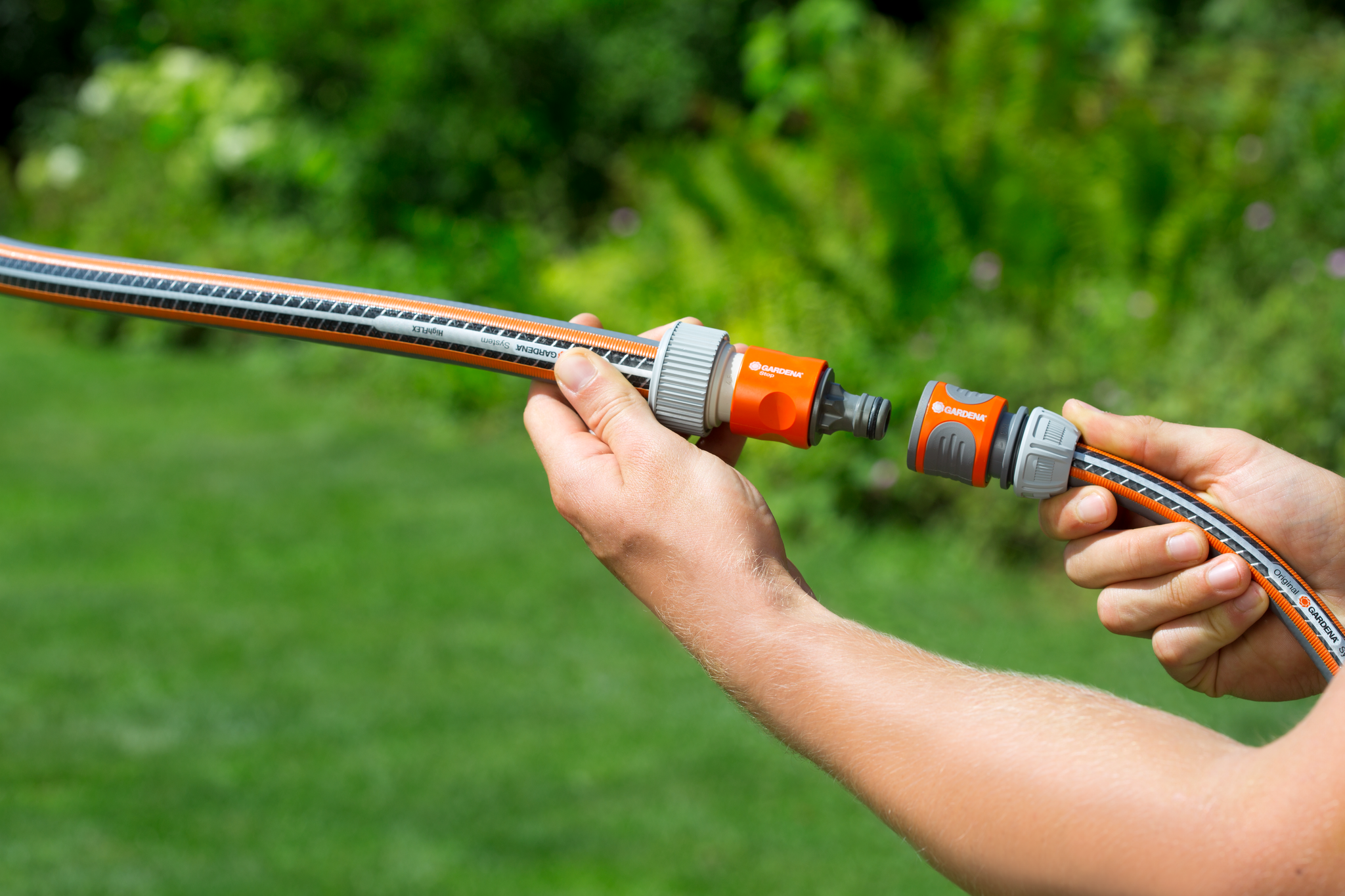 A person connecting a Gardena garden hose with a quick connector in a garden setting.