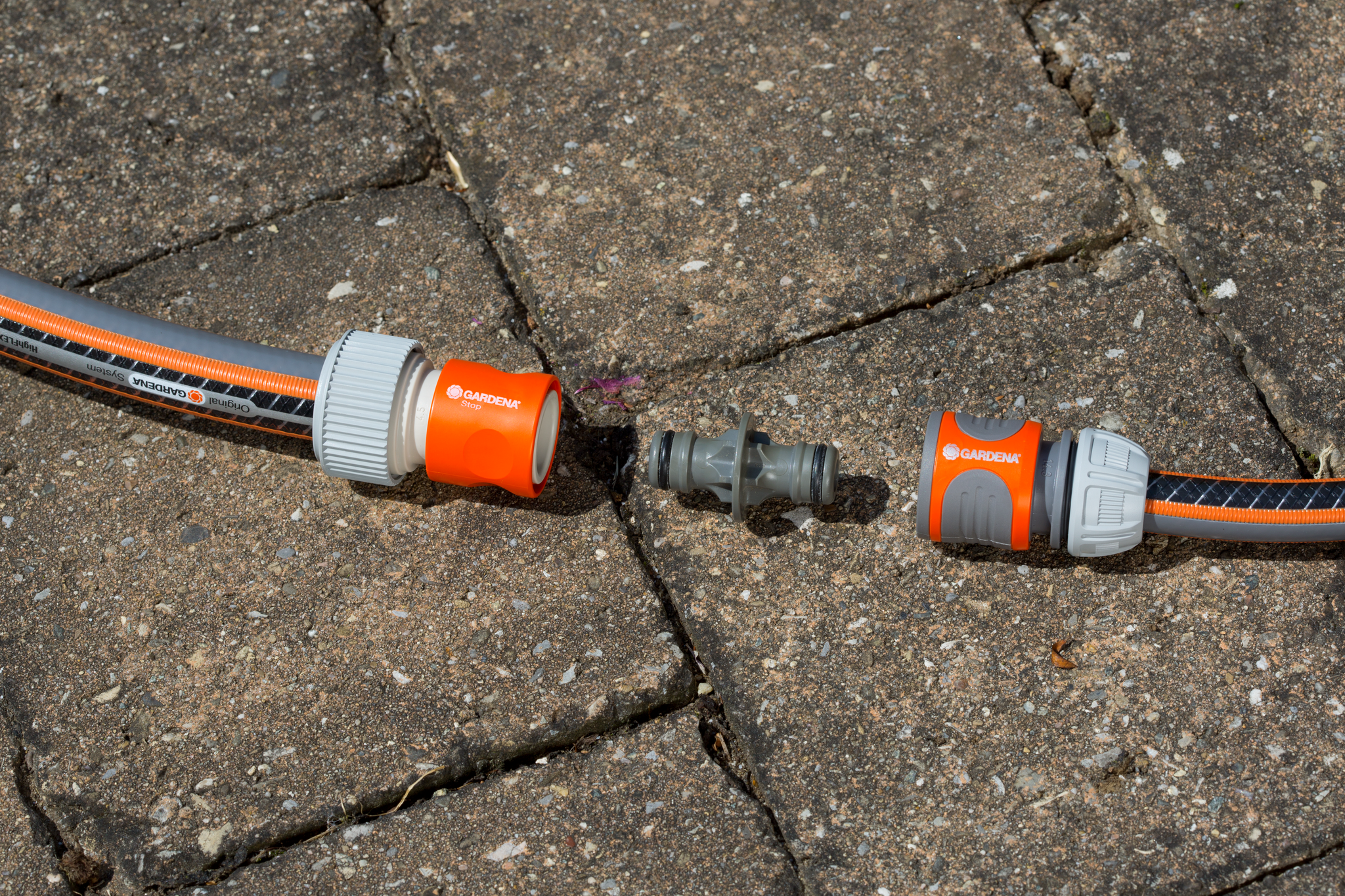 Gardena hose connectors and a coupler on a stone pavement.