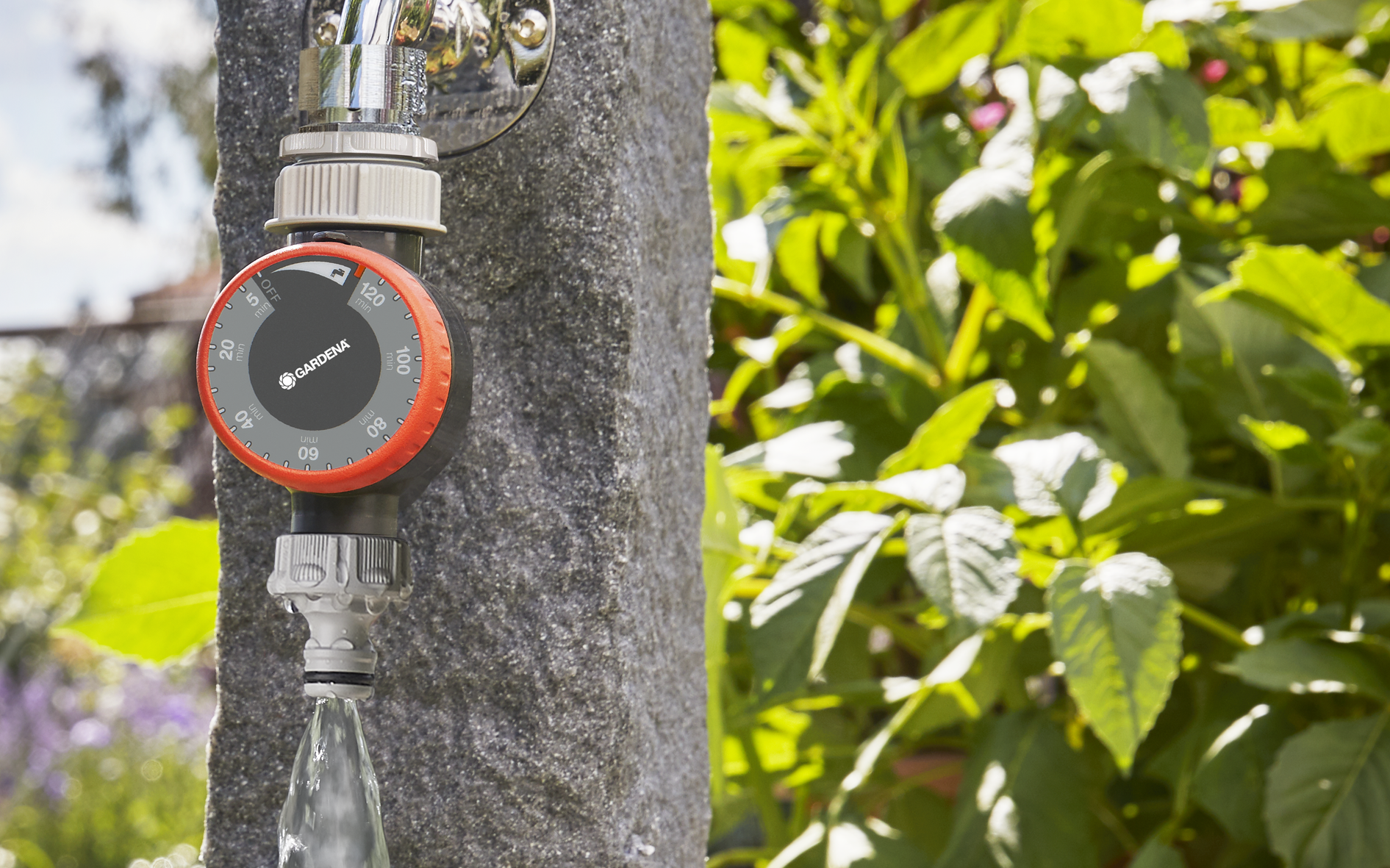 Gardena water timer attached to an outdoor faucet, with water flowing into a garden.