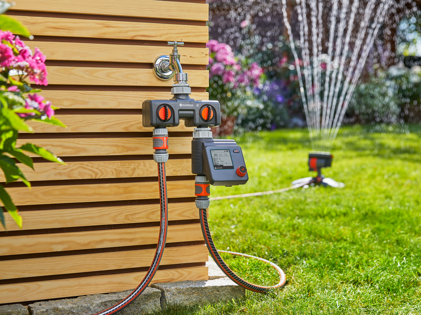 A Gardena water control system connected to a garden tap, with a sprinkler in the background.
