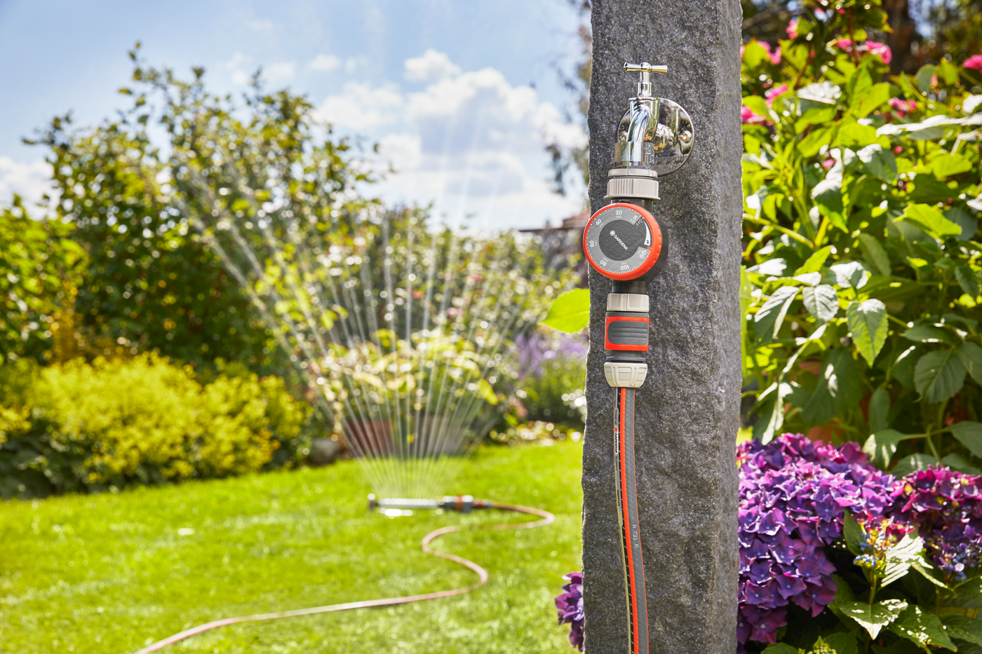 Gardena water timer attached to a garden tap, with a sprinkler watering the lawn.