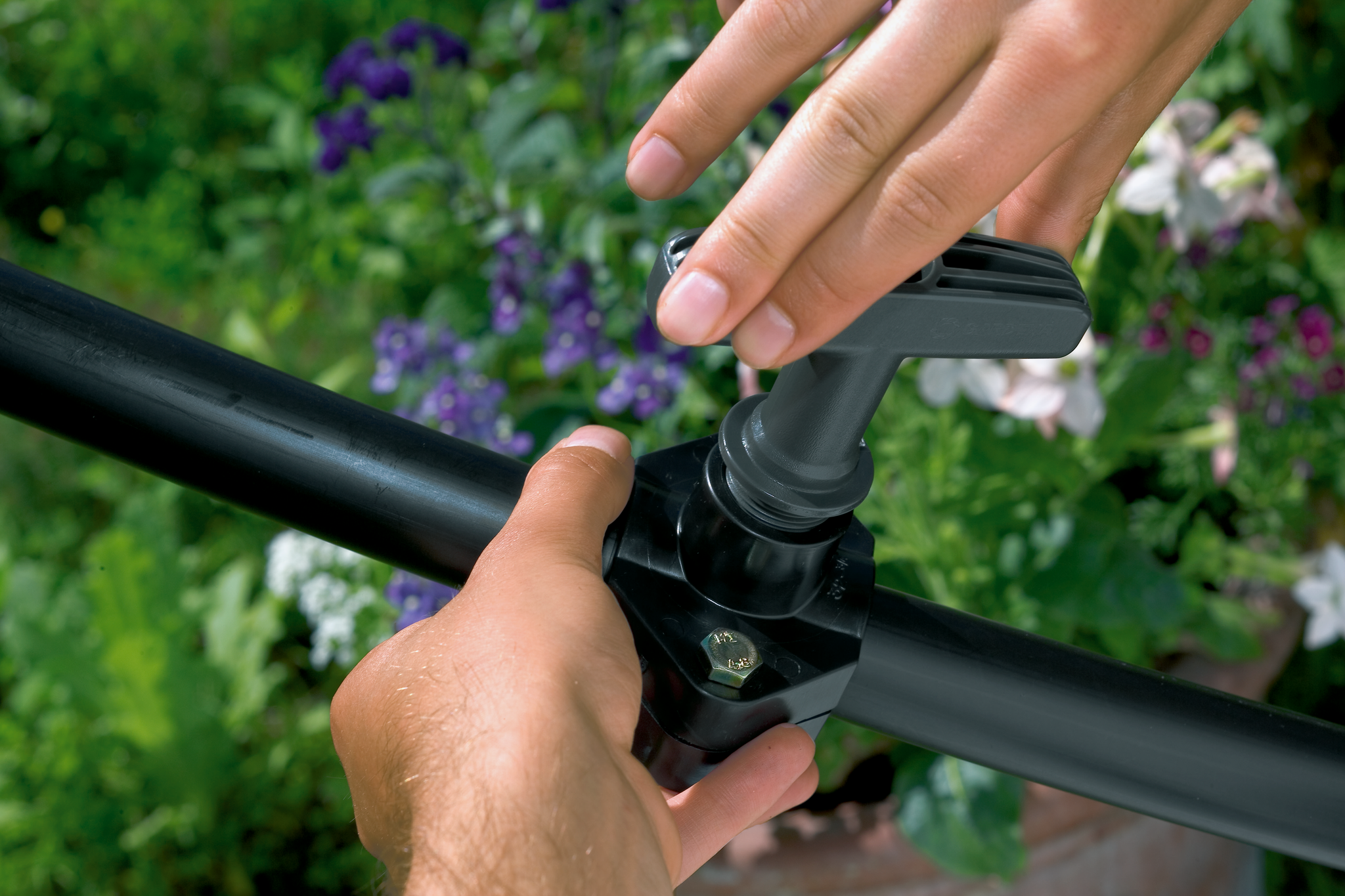 A person adjusting a Gardena irrigation valve in a garden setting.