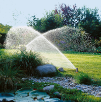 Garden sprinkler system watering a lush green lawn with decorative rocks and plants., miniatuur 2