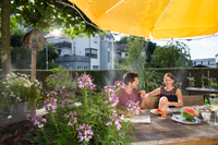 Two people sitting at a wooden table in a garden, enjoying watermelon under a large yellow umbrella., miniatuur 5