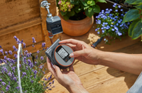A person adjusting a Gardena irrigation control device in a garden setting., miniatuur 3