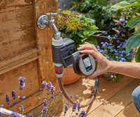 A person adjusting a Gardena water timer attached to a garden tap, surrounded by plants., miniatuur 5