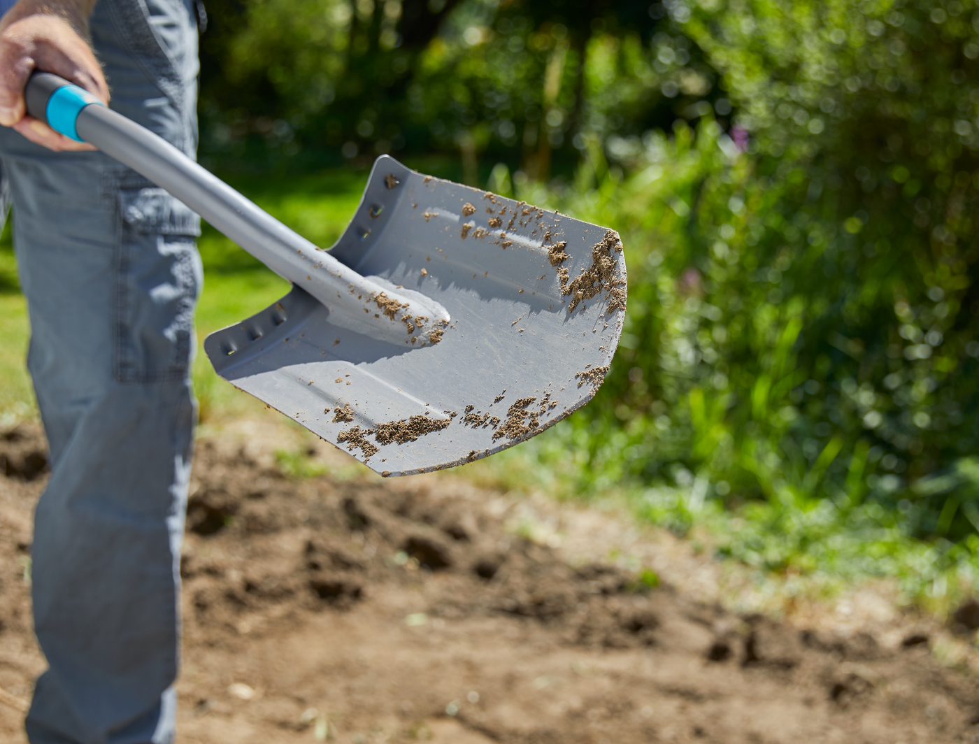 A person holding a shovel with soil in a garden setting.