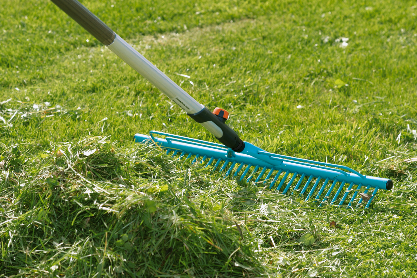 A Gardena rake being used to gather grass clippings on a lawn.