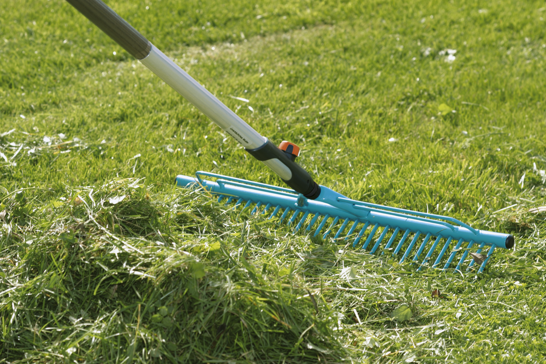 A Gardena rake being used to gather grass clippings on a lawn.