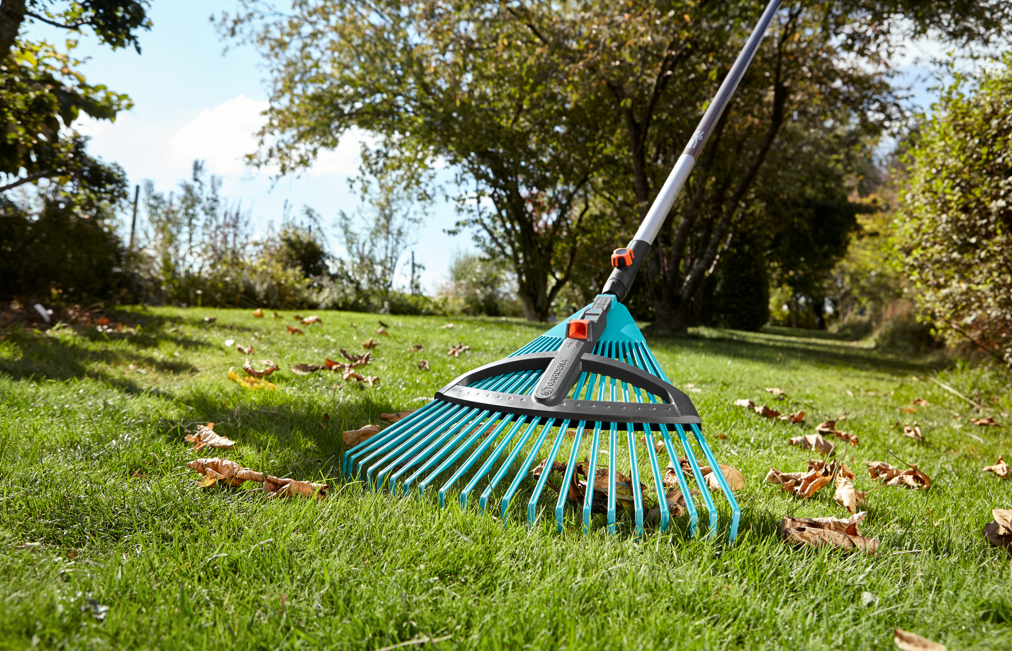 A Gardena rake being used to gather fallen leaves on a grassy lawn.