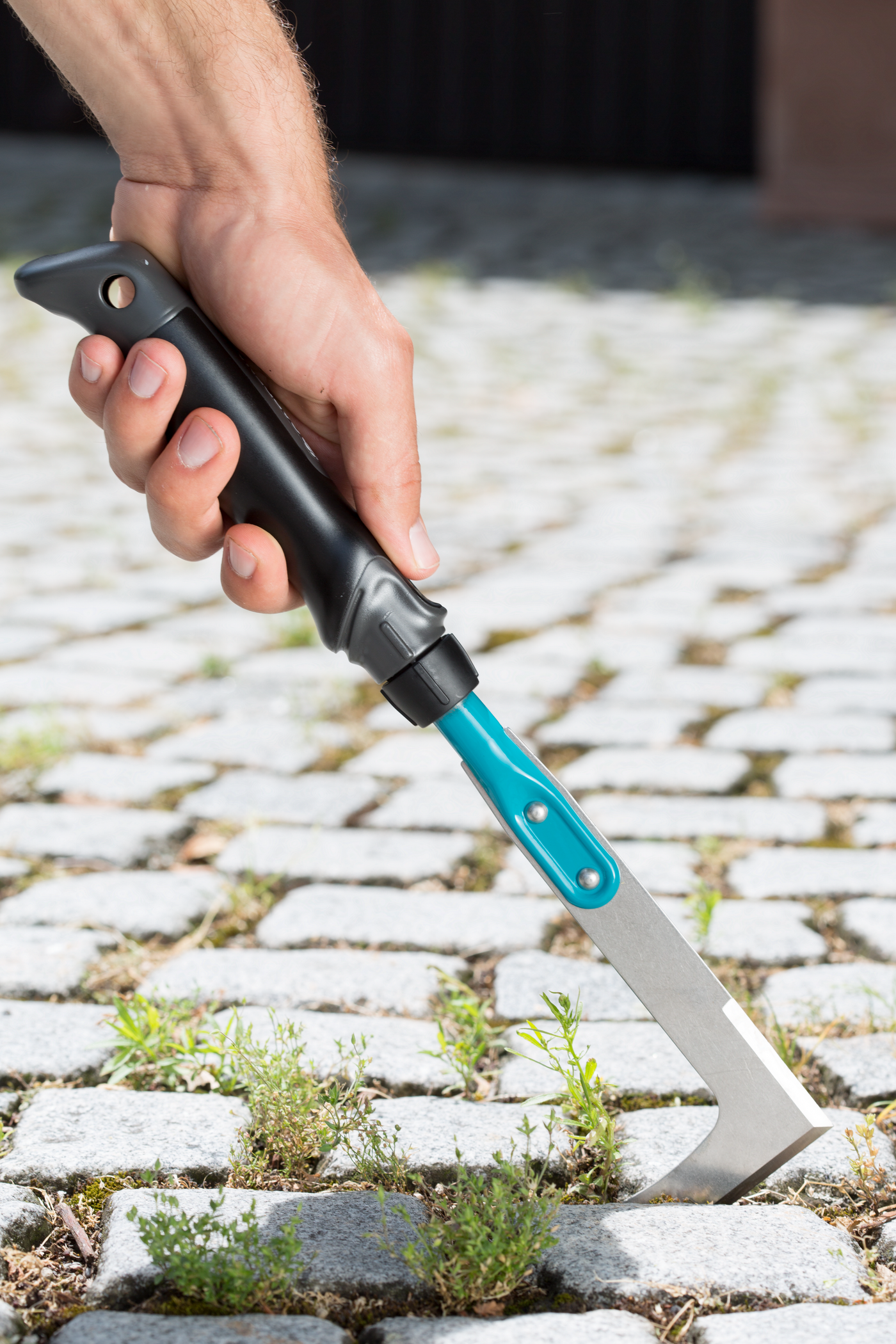A person using a handheld tool to remove weeds from between cobblestones.
