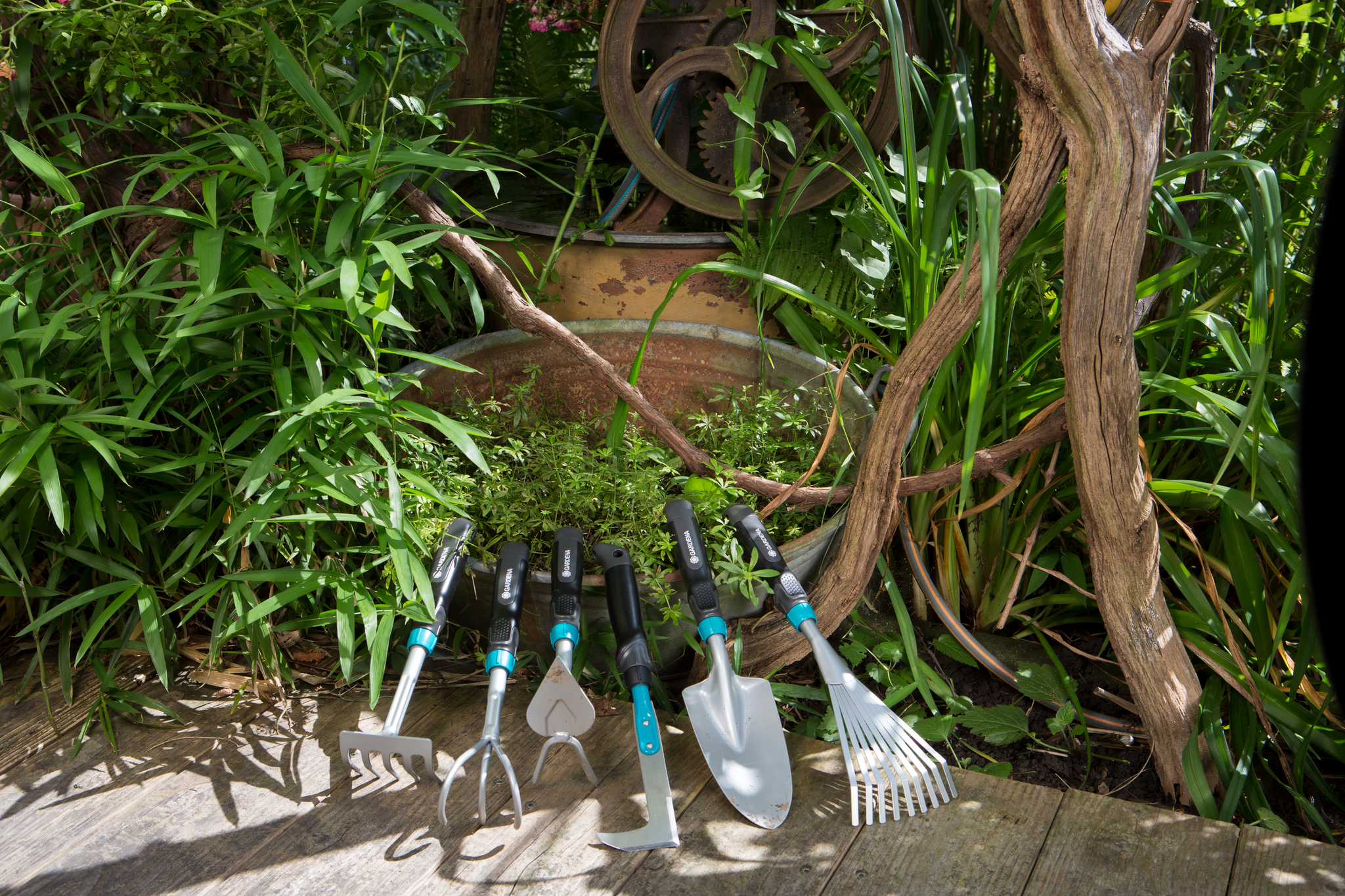A set of Gardena gardening hand tools displayed on a wooden deck surrounded by lush greenery.