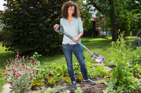 A person holding a garden hoe, standing in a vibrant garden with various plants and flowers., miniatuur 2