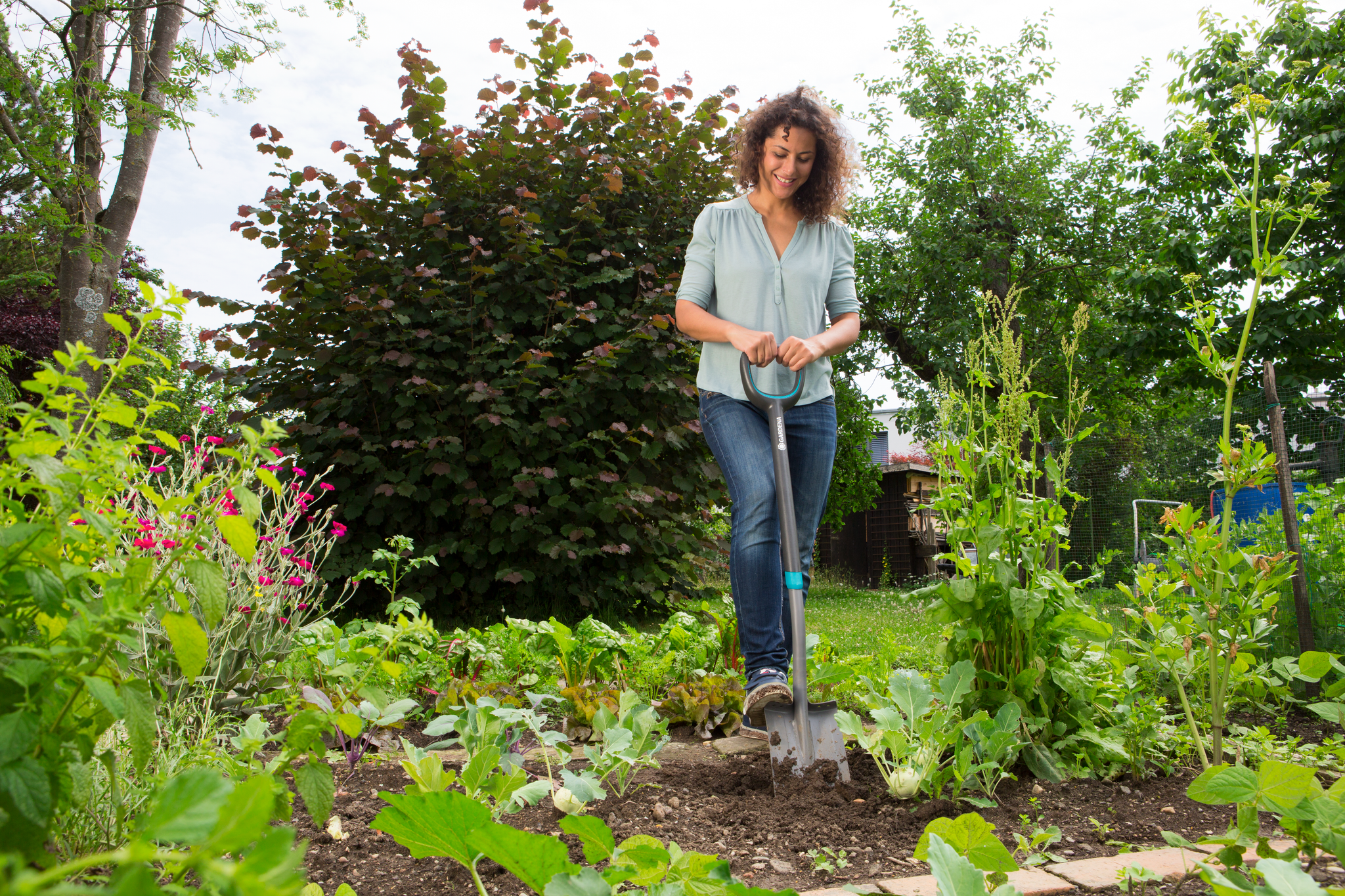 A person using a Gardena garden shovel to work in a lush garden.