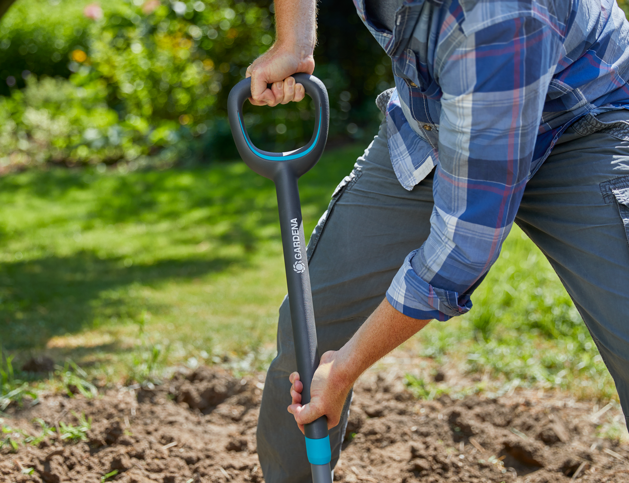A person using a Gardena shovel to dig soil in a garden.
