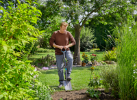 A person using a shovel to dig in a garden surrounded by lush greenery., miniatuur 3
