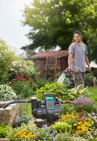 A person watering plants in a garden using a hose, with a water pump visible in the foreground., miniatuur 3