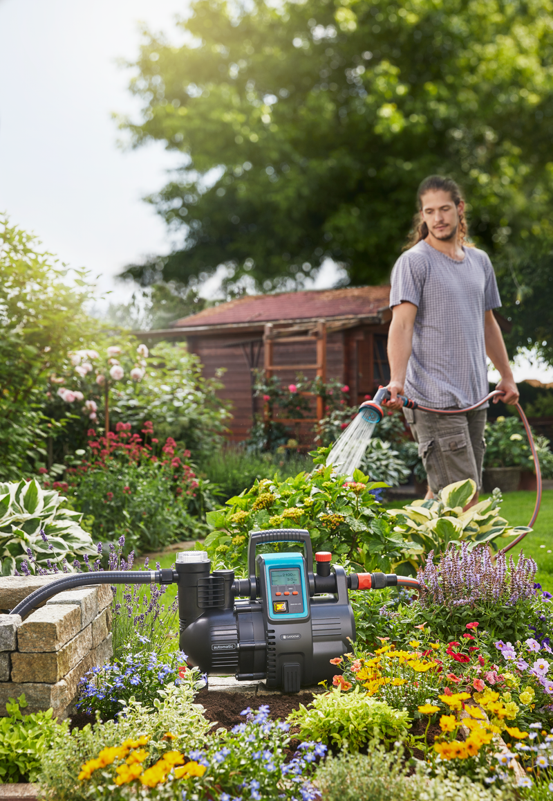 A person watering plants in a garden using a hose, with a water pump visible in the foreground., afbeelding 3 Filterpomp