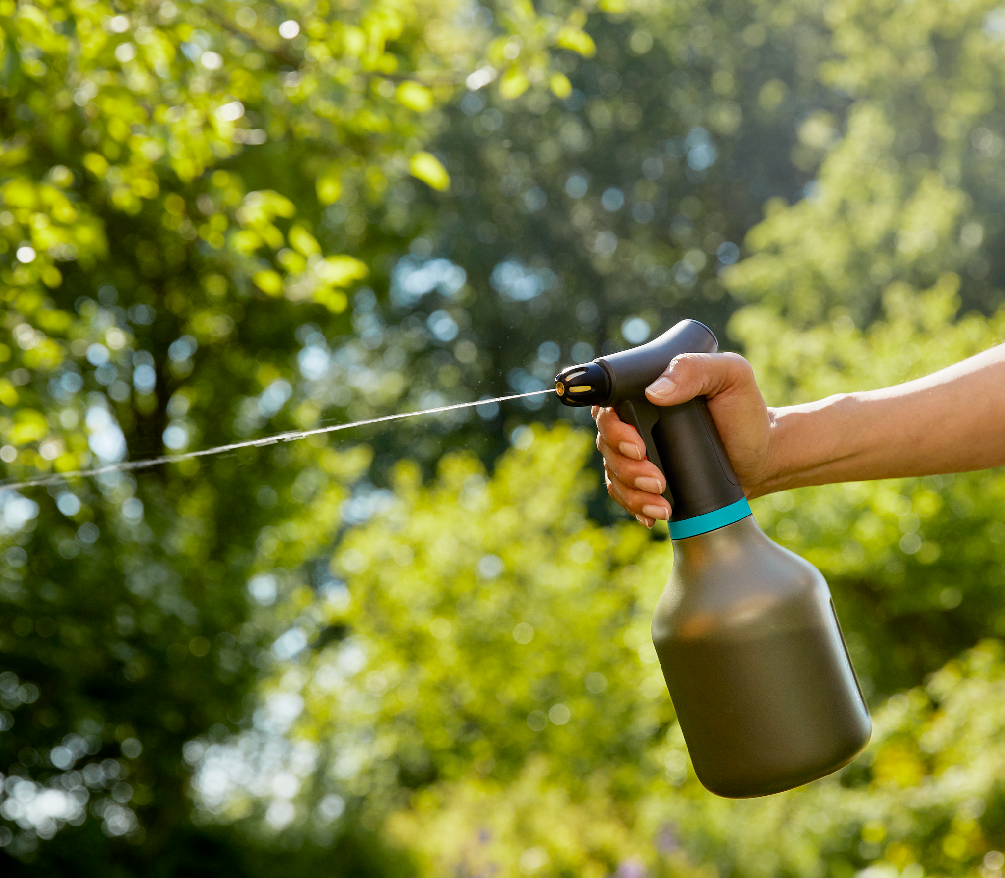 A person using a garden spray bottle in a lush garden setting.