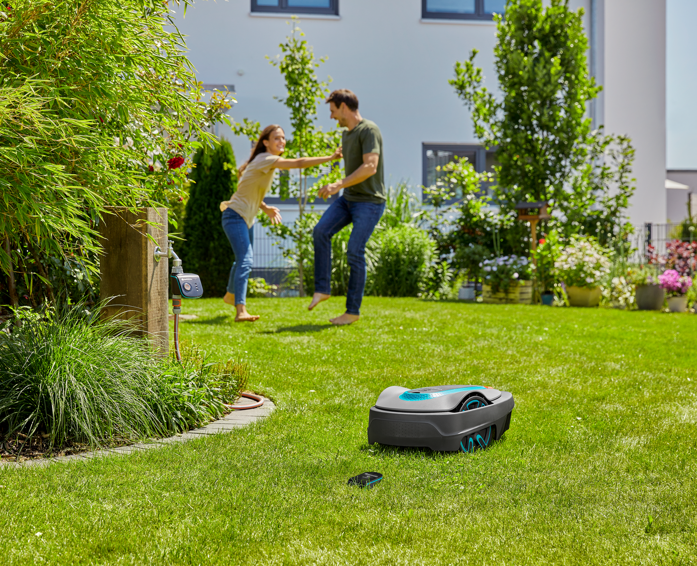 A robotic lawn mower operating in a garden while two people interact in the background.
