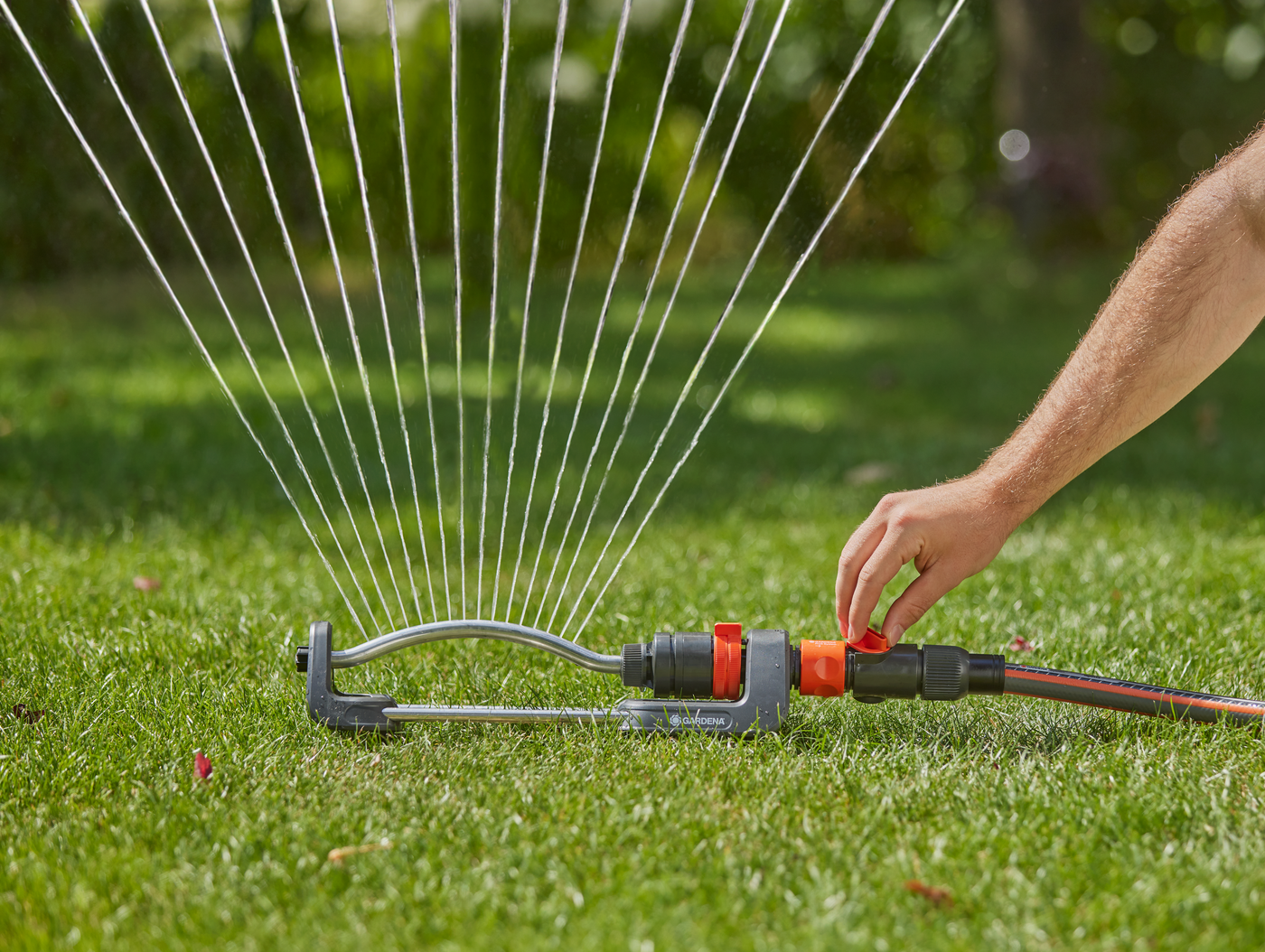 A person adjusting a garden sprinkler on a lawn.