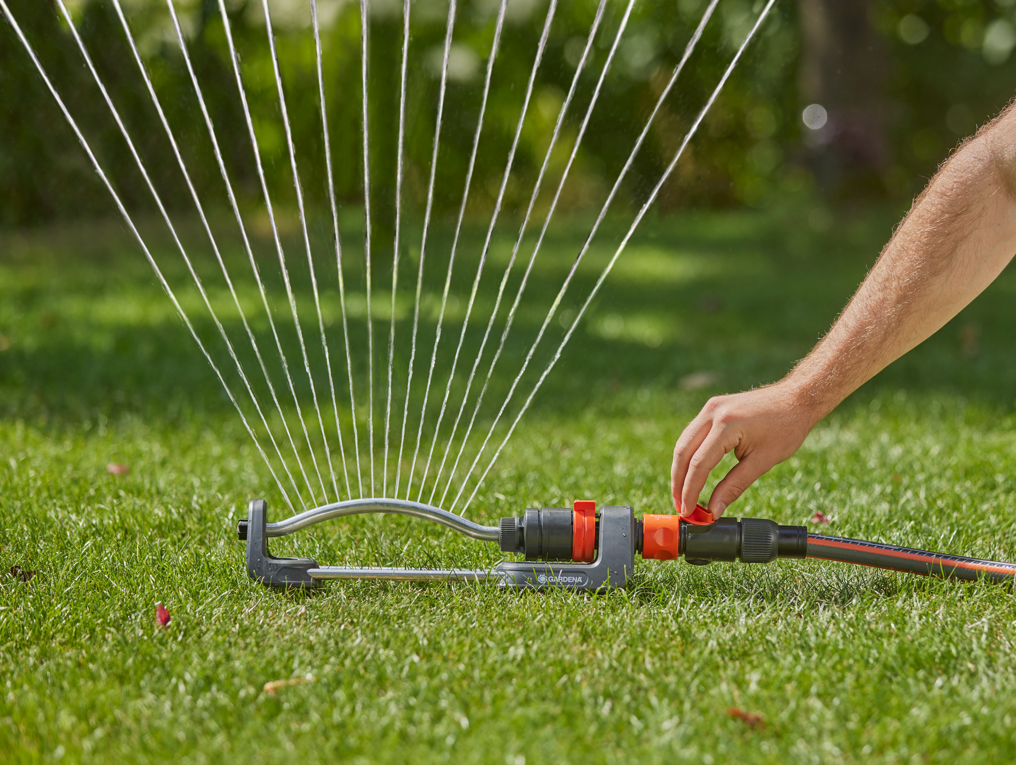 A person adjusting a garden sprinkler on a lawn.