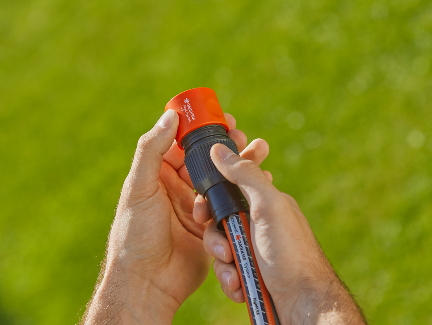 A person holding a Gardena hose connector in a garden setting.