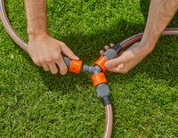Hands connecting garden hoses using a three-way connector on grass., miniatuur 2