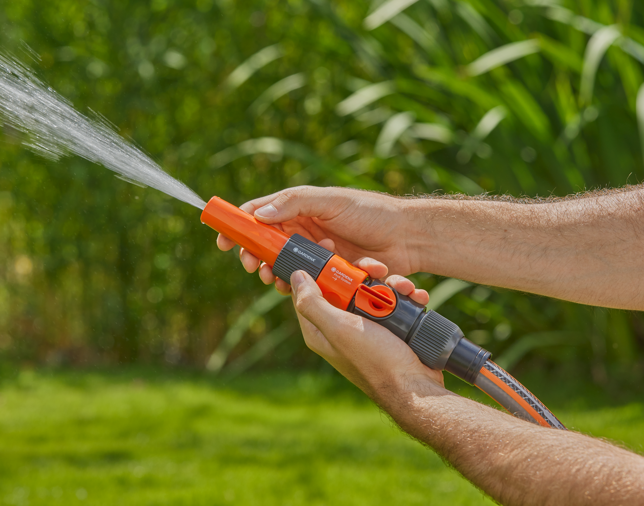 A person adjusting a Gardena garden hose nozzle, spraying water in a garden.