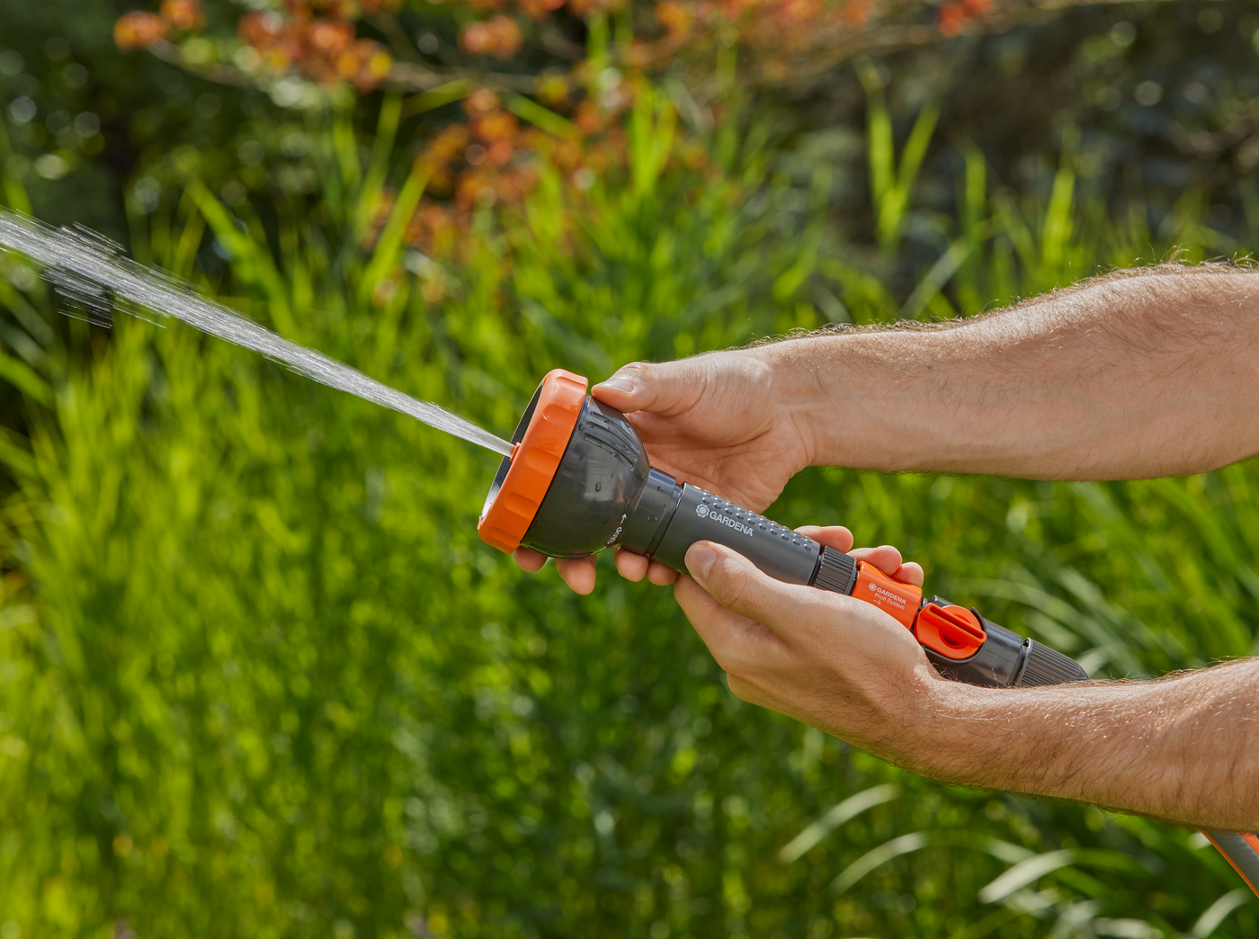 A person adjusting a garden hose nozzle, spraying water in a garden setting.