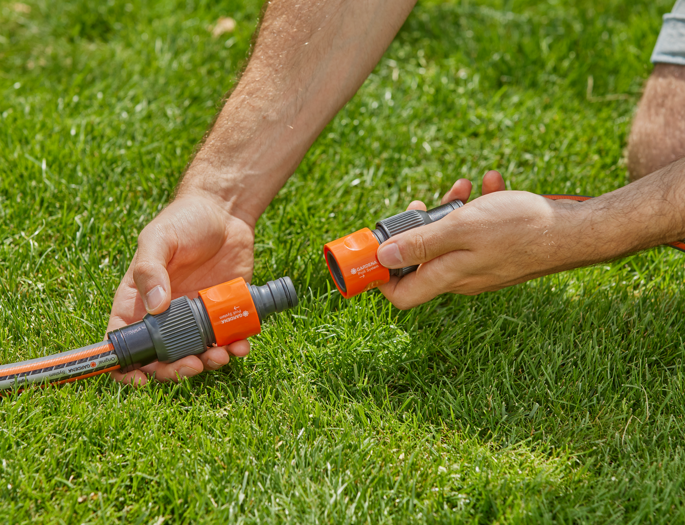 A person connecting two Gardena hose connectors on a grassy lawn.