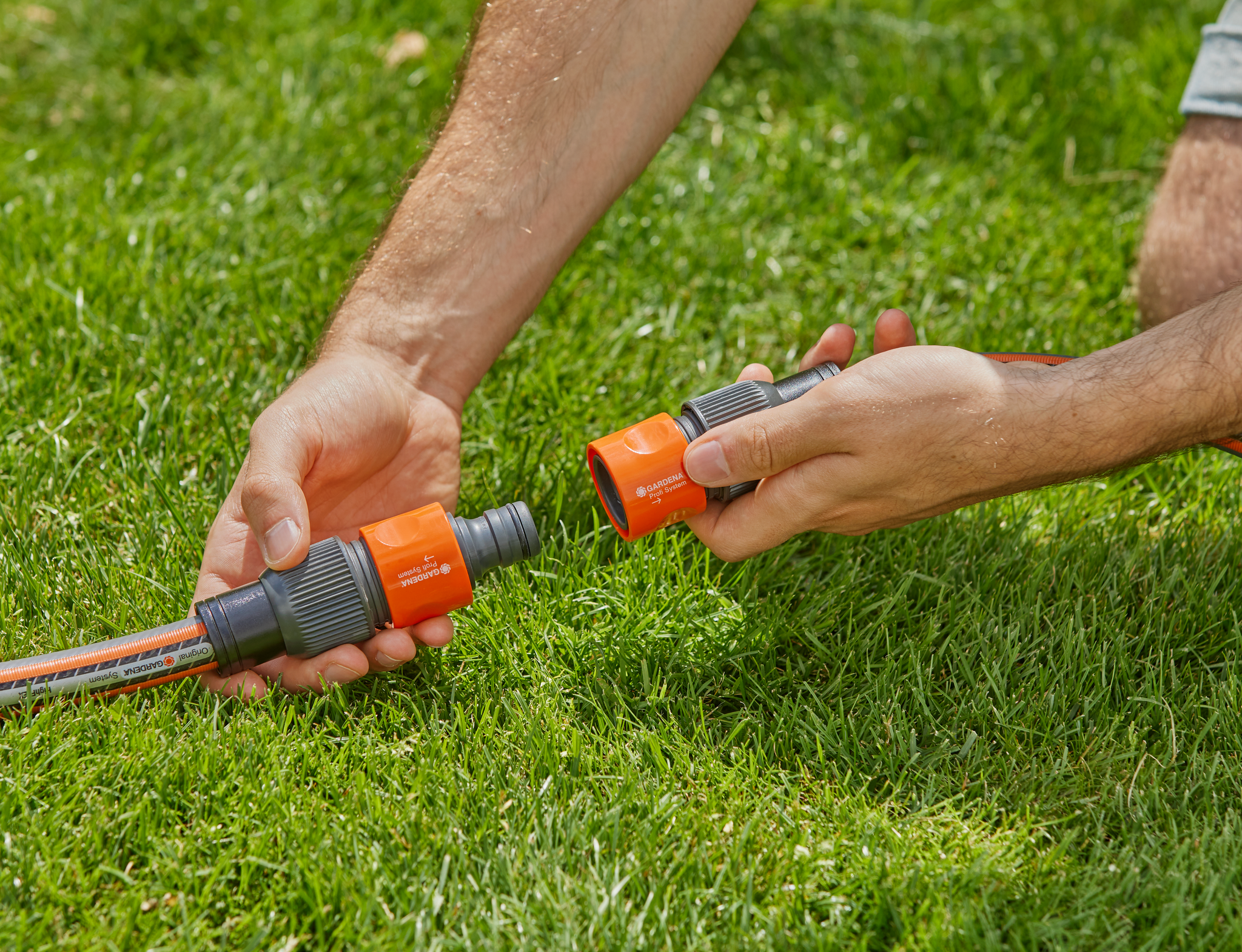 A person connecting two Gardena hose connectors on a grassy lawn.